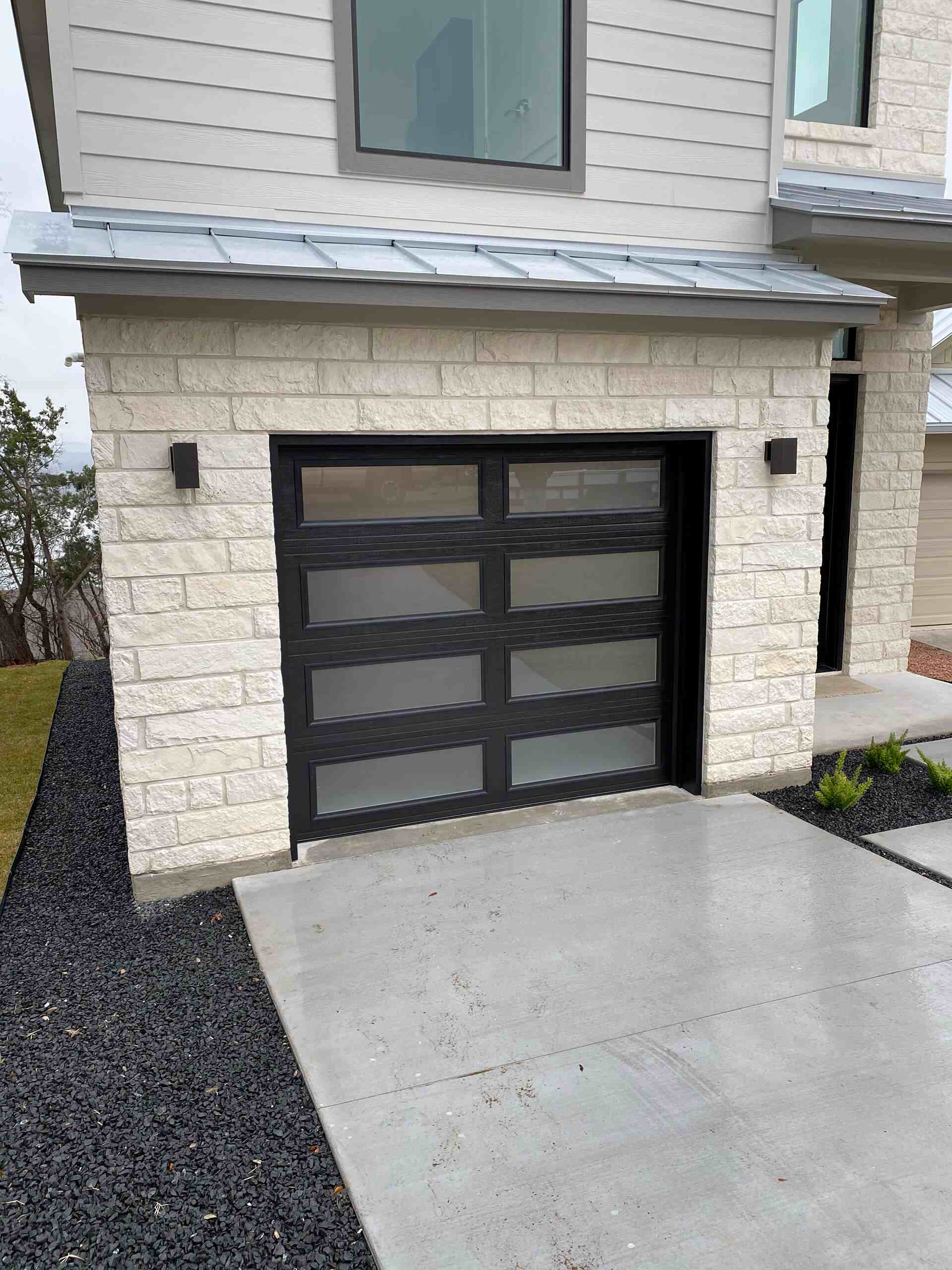 Modern glass-panel garage door installed by Door Pro Plus on a Hill Country stone home