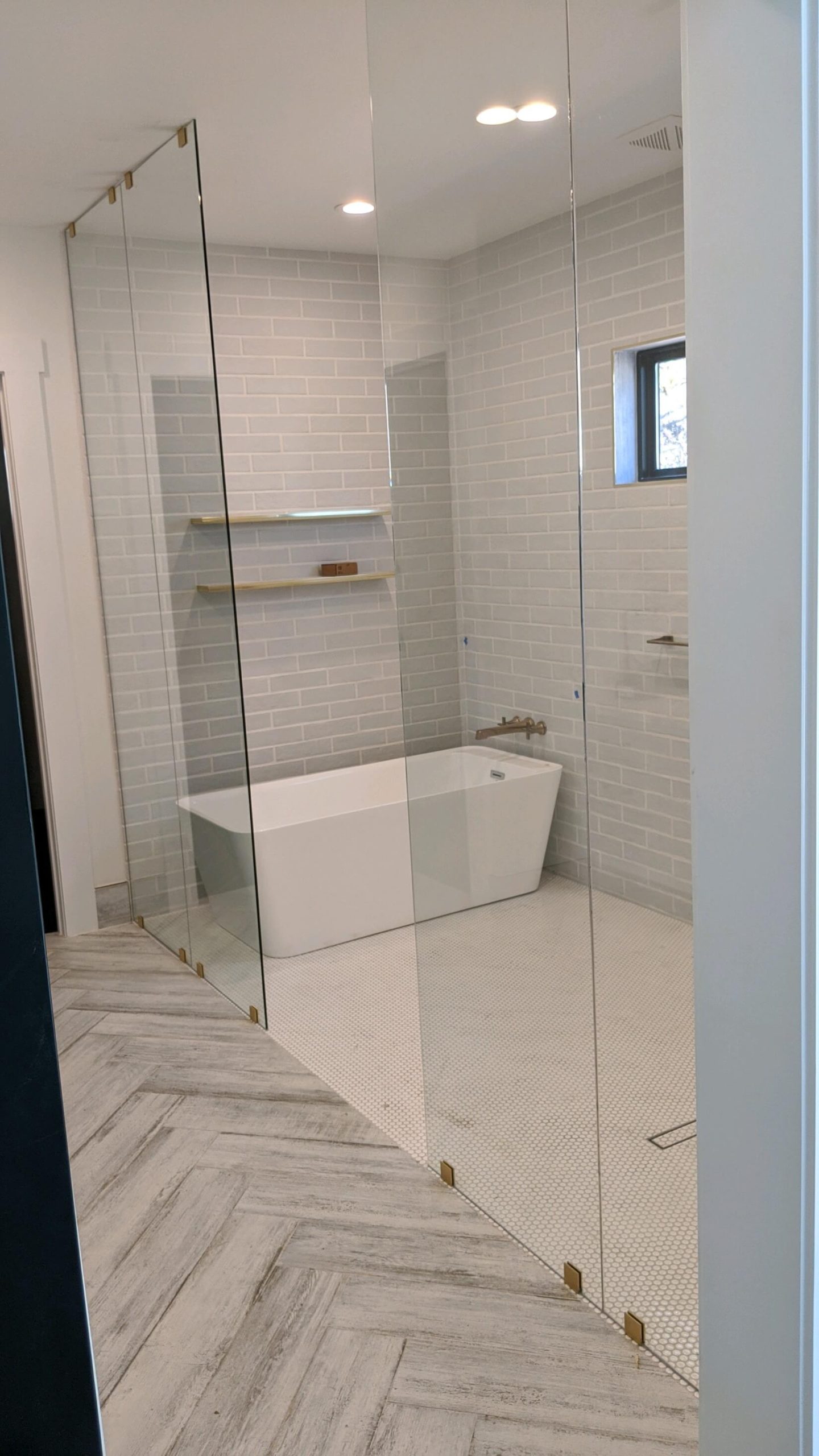 Frameless glass shower enclosure with brass hardware next to a freestanding tub, installed by Door Pro Plus in a Marble Falls, TX master bathroom