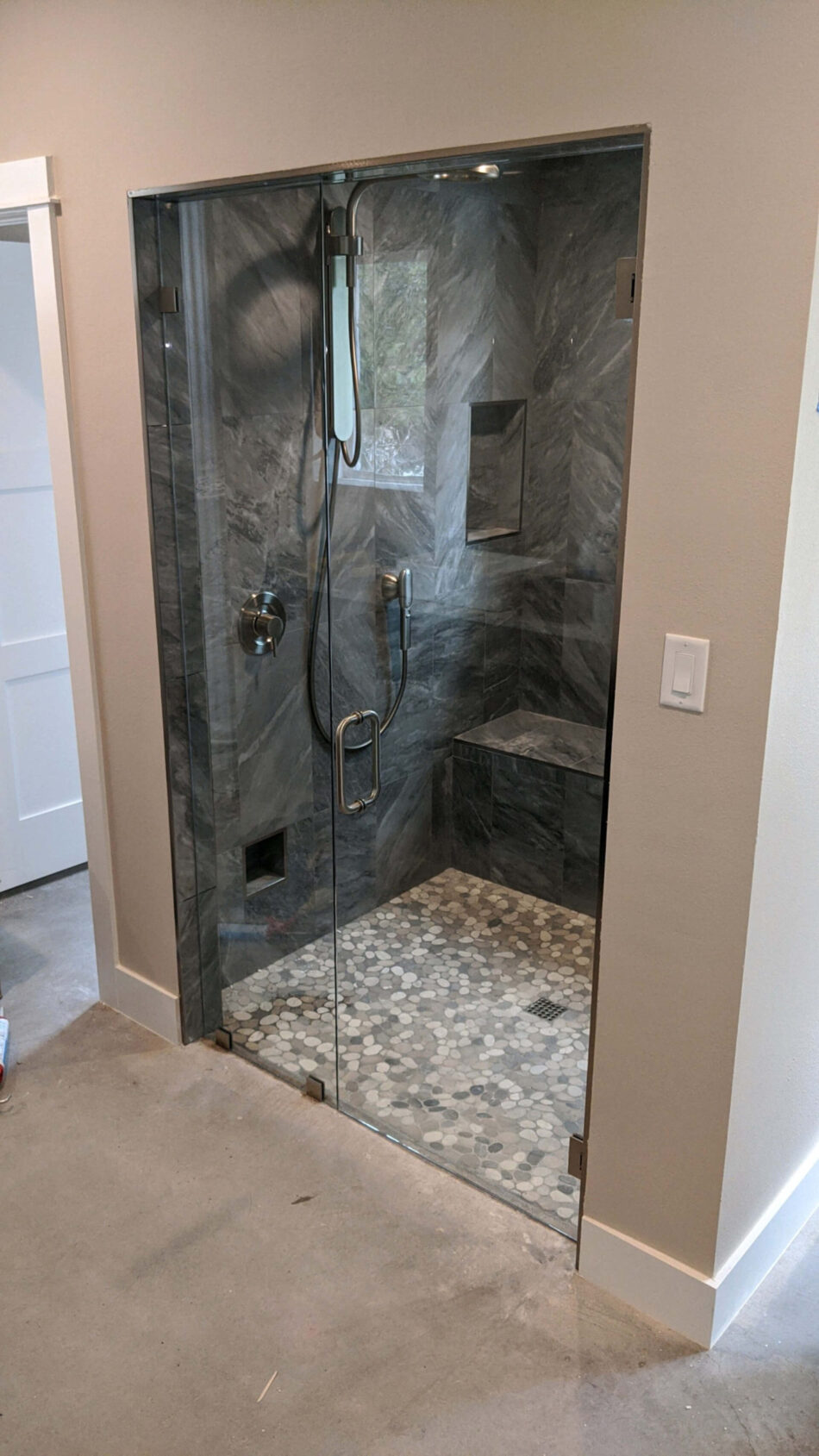 Frameless glass shower enclosure with gray stone tile and a built-in bench seat, installed by Door Pro Plus near Marble Falls, TX